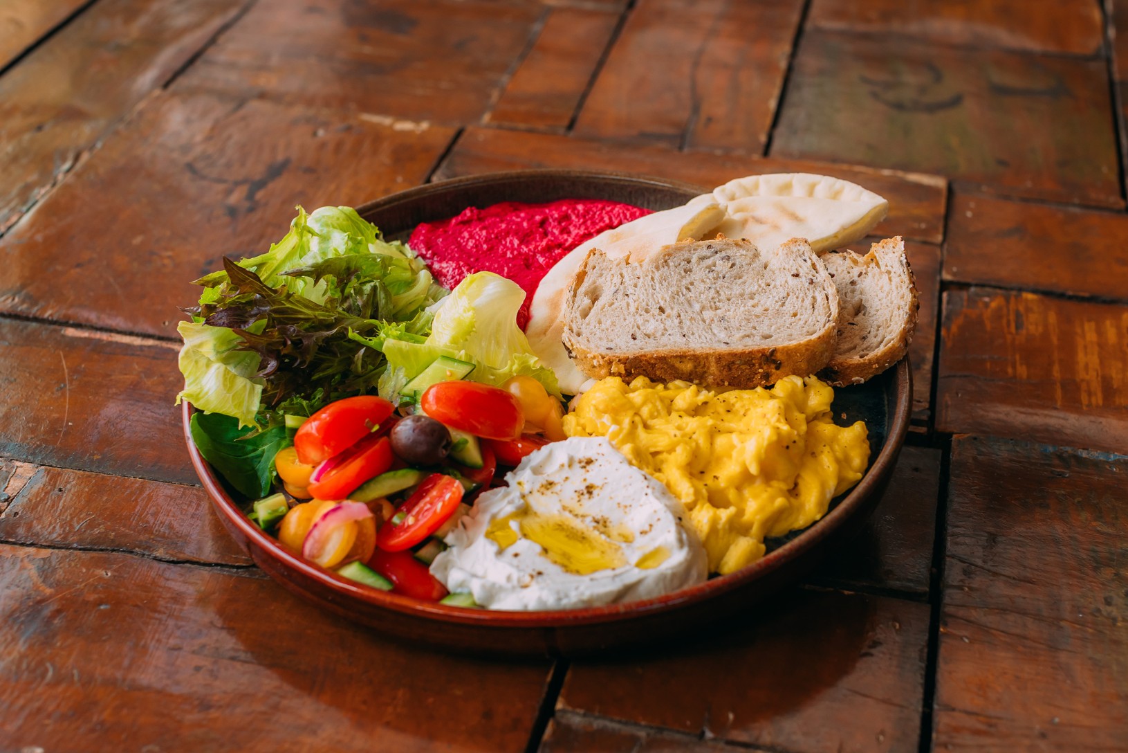 Prato com hummus de beterraba, coalhada seca, ovos mexidos, salada mediterrânea e pães